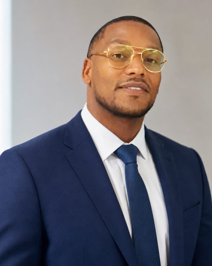 Martell Rogers, wearing a navy suit and gold-rimmed glasses